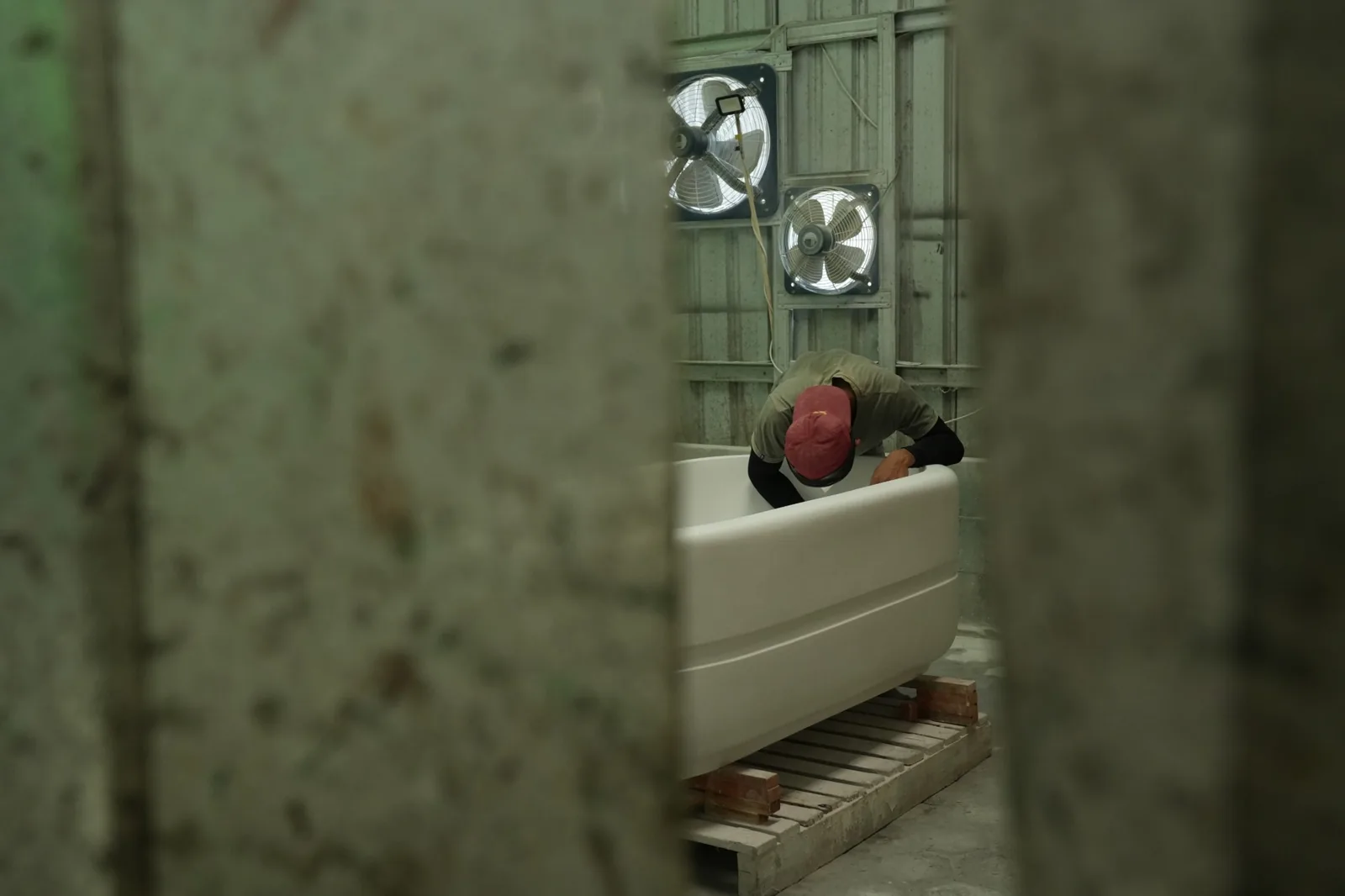 A maker finishing a terrazzo bathtub, seen through the workshop