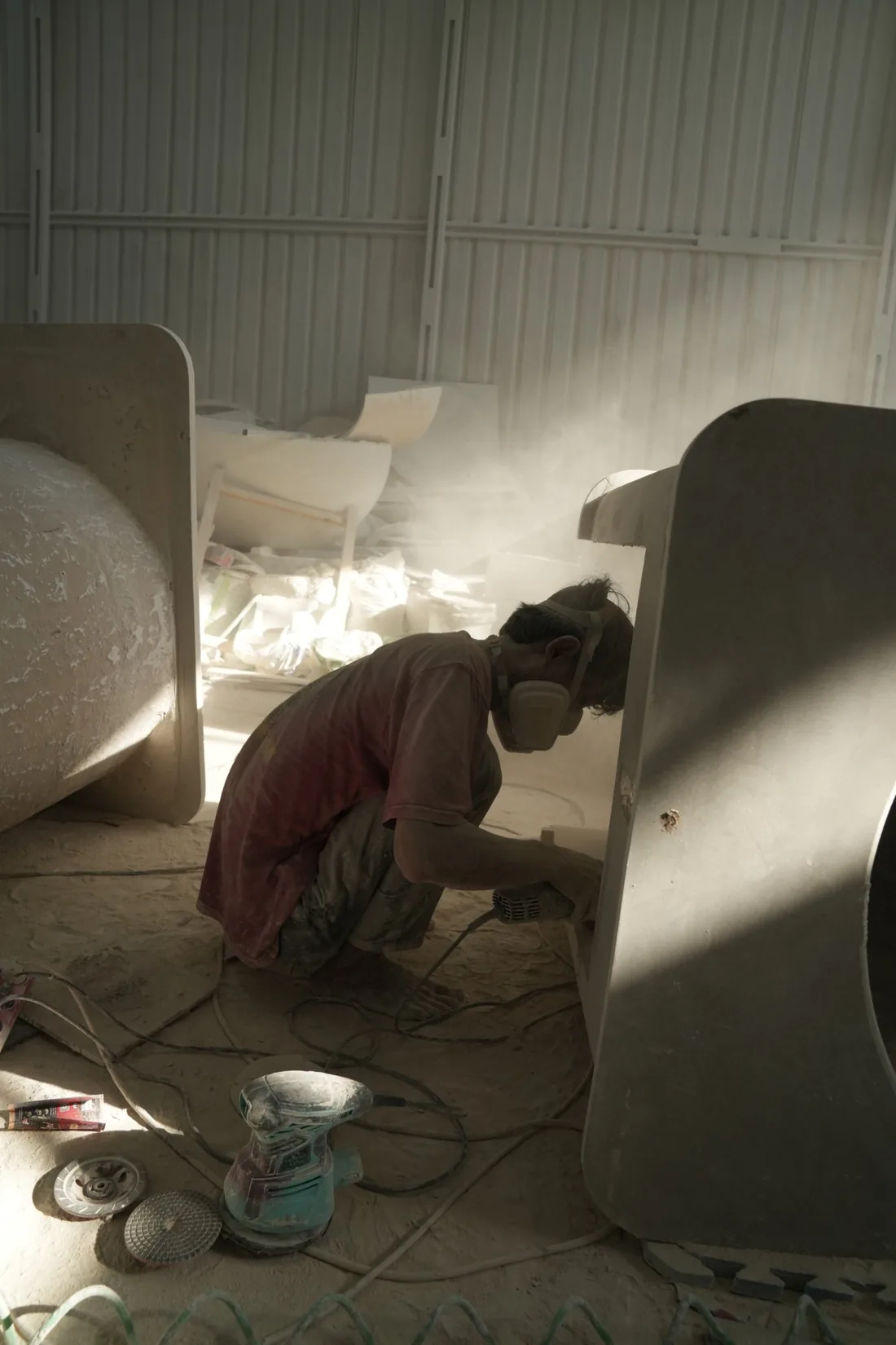 A maker finishing a terrazzo bathtub by hand in raking light